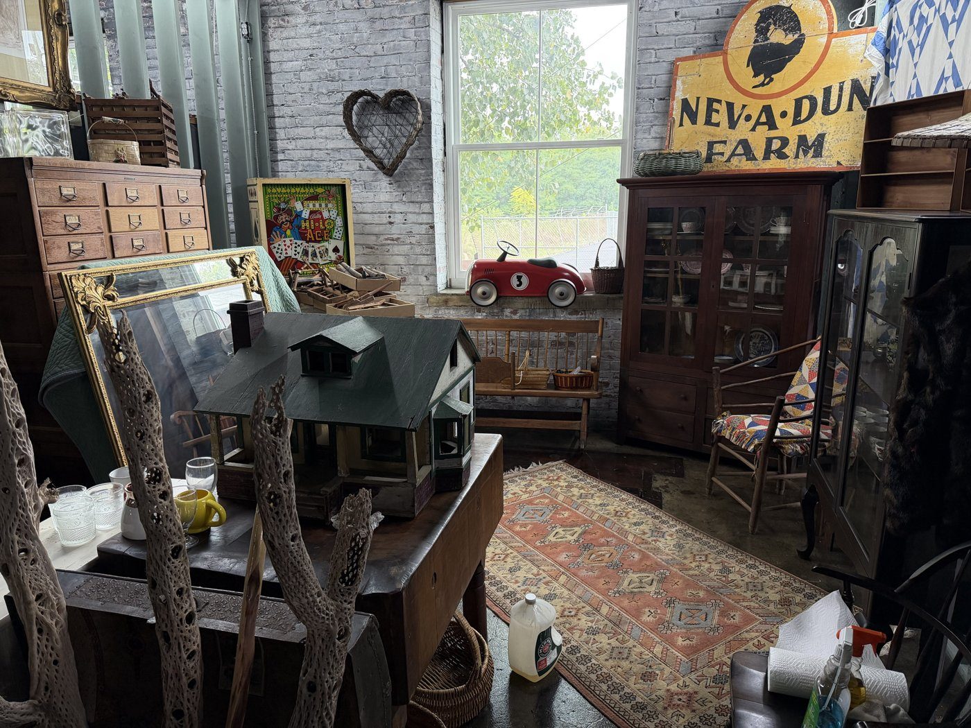 A corner of the shop with a wooden dollhouse, a red pedal car in the window and a vintage farm sign